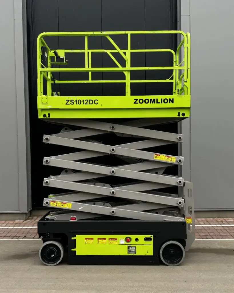 Alt= Een schaarhoogwerker staat voor een gebouw en heeft een hoogte van 12 meter